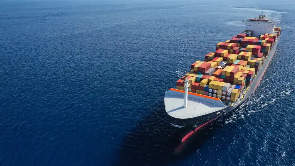 Aerial view of a massive container ship sailing in the ocean, explaining what is economy shipping for international trade.