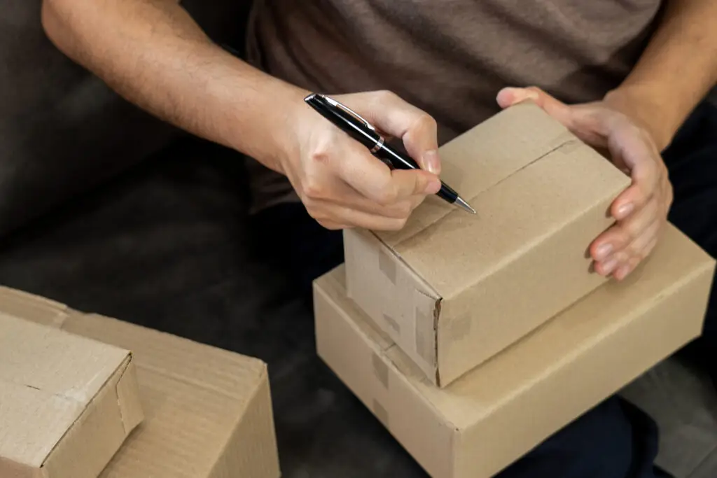 Person labeling cardboard boxes for shipping, showing the difference between courier and parcel delivery services