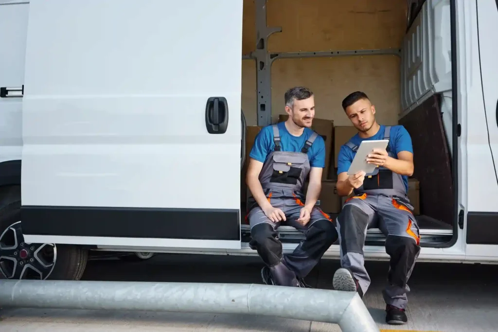 Two delivery workers reviewing a tablet while sitting in a delivery van, illustrating what is outbound delivery services and efficient local courier operations