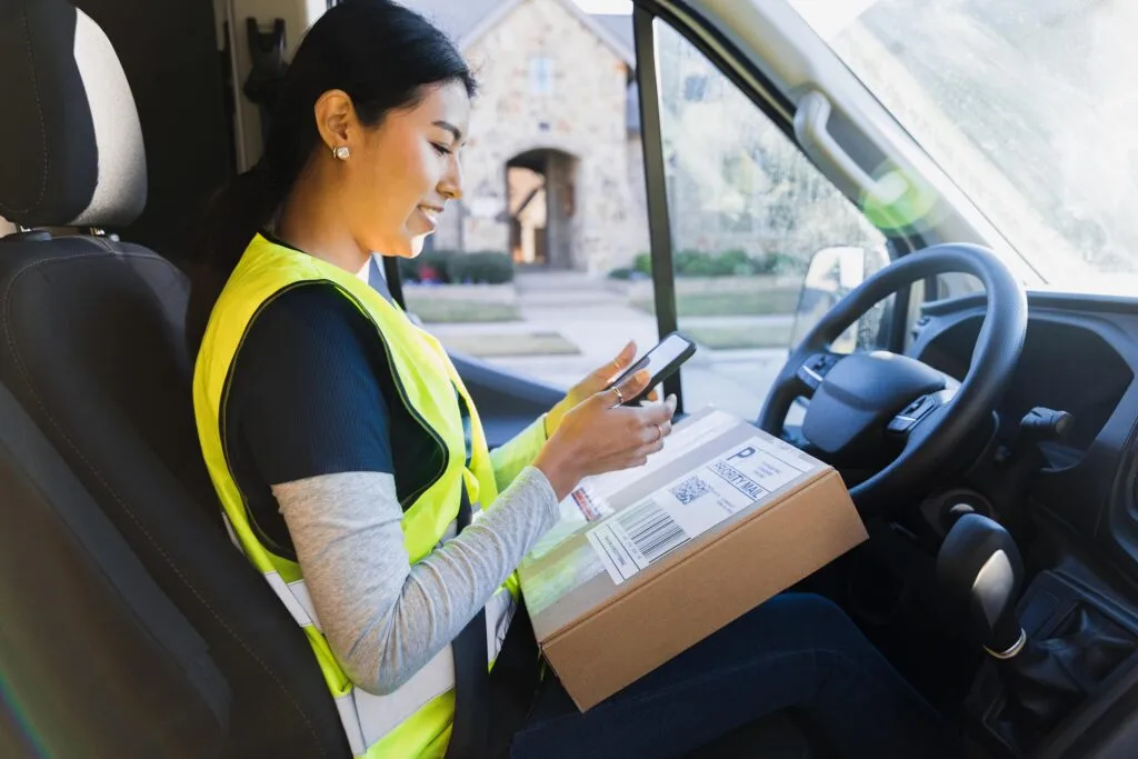 Courier driver delivering a package while using a mobile device, illustrating how business benefit from delivery services.