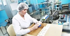 Pharmaceutical worker in a hairnet and white coat packing medicine boxes into a cardboard carton, illustrating what is pharmaceutical logistics